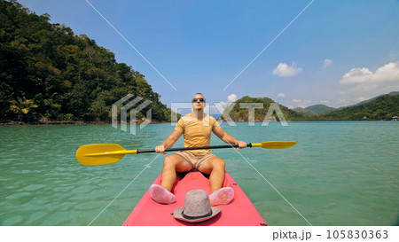 Man with sunglasses and hat rows pink plastic canoe along sea ag 105830363