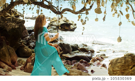 Pretty woman swinging on a swing on a tropical beach, on shores of the turquoise sea. Concept travel, walks, rest in sea, tropical resort coastline relaxation traveling tourism summer holidays. 105830369