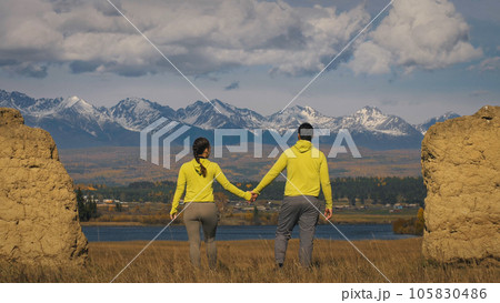 Man and woman in yellow green sportswear. Lovely couple of travelers hug and kiss near old stone enjoying highland landscape. 105830486