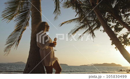 Woman drinking pineapple cocktail Pina Colada near palm tree, in 105830499