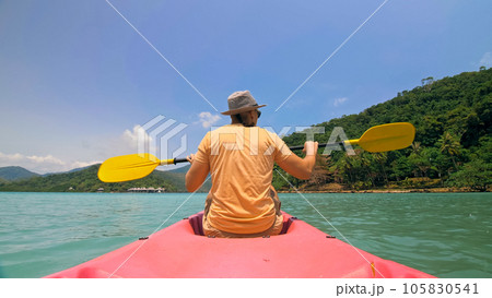 Man with sunglasses and hat rows pink plastic canoe along sea ag Man with sunglasses and hat rows pink plastic canoe along sea ag 105830541