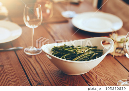 Thanksgiving, green beans and food with a place setting on a dining room table for a celebration event. Party, dish and dinner with a bowl on a wooden surface in celebration or holiday tradition Thanksgiving, green beans and food with a place setting on a dining room table for a celebration event. Party, dish and dinner with a bowl on a wooden surface in celebration or holiday tradition 105830839