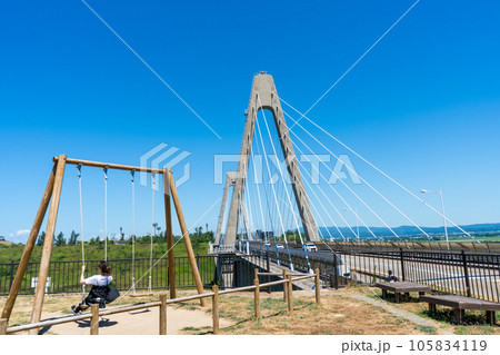 晴れの夏空と日本海と河北潟を繋ぐ河北潟放水路に架かる内灘大橋と道の駅のブランコ｜石川県河北郡内灘町 105834119