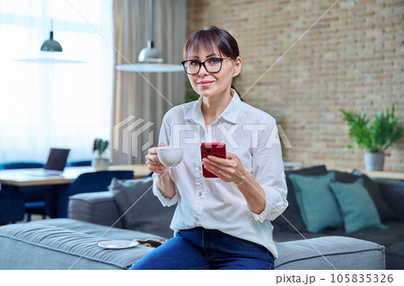 Middle aged woman using smartphone, having cup of coffee at home 105835326