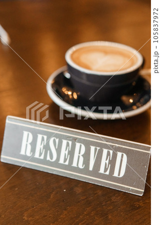 Coffee cup with a heart pattern in a blue cup on a wooden background. A sign with the inscription - reserved. Coffee cup with a heart pattern in a blue cup on a wooden background. A sign with the inscription - reserved. 105837972