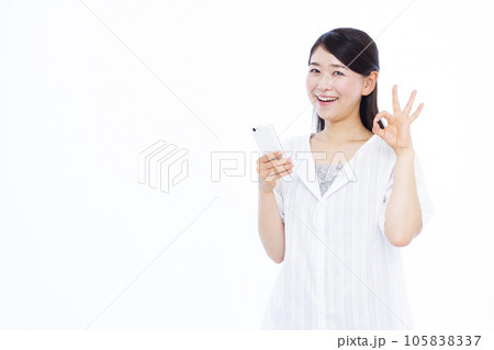 白い背景の前でスマホを持ちOKサインをしている30代の女性 白い背景の前でスマホを持ちOKサインをしている30代の女性 105838337