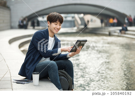 A young man working on a laptop in a park with a river 105840192