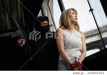 Masked criminal with gun and women as hostages standing looking out of window 105842422