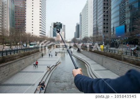 A man's hand holding a camera against a river-flowing city background A man's hand holding a camera against a river-flowing city background 105843545