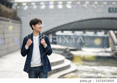 a young man taking a walk in a park with a river in the city a young man taking a walk in a park with a river in the city 105843669