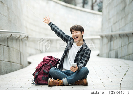 A young man sitting on the street taking pictures with a smartphone camera while traveling A young man sitting on the street taking pictures with a smartphone camera while traveling 105844217