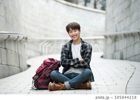 A young man sitting on the street taking pictures with a smartphone camera while traveling A young man sitting on the street taking pictures with a smartphone camera while traveling 105844218