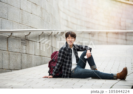 A young man sitting on the street taking pictures with a smartphone camera while traveling 105844224
