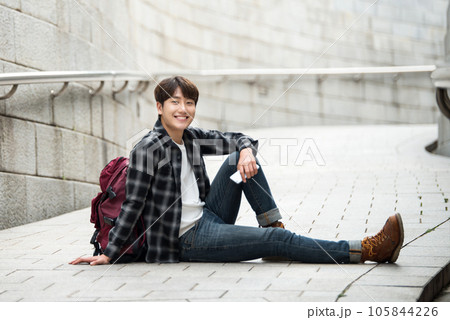 A young man sitting on the street taking pictures with a smartphone camera while traveling A young man sitting on the street taking pictures with a smartphone camera while traveling 105844226