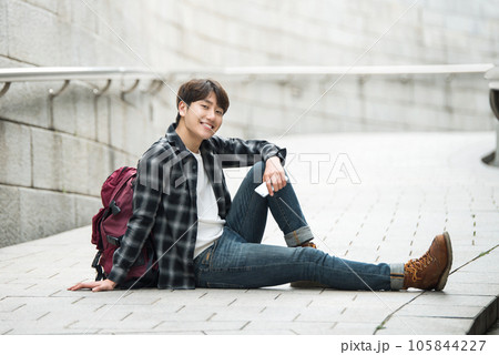 A young man sitting on the street taking pictures with a smartphone camera while traveling A young man sitting on the street taking pictures with a smartphone camera while traveling 105844227