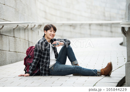 A young man sitting on the street taking pictures with a smartphone camera while traveling A young man sitting on the street taking pictures with a smartphone camera while traveling 105844229