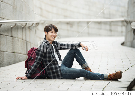 A young man sitting on the street taking pictures with a smartphone camera while traveling A young man sitting on the street taking pictures with a smartphone camera while traveling 105844235