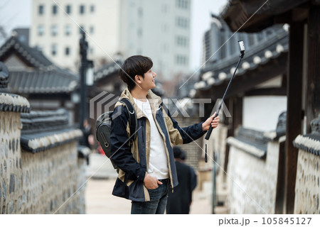 A young man traveling around a traditional village and taking pictures with a smartphone camera A young man traveling around a traditional village and taking pictures with a smartphone camera 105845127