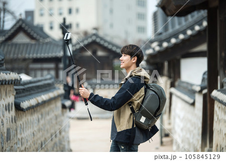 A young man traveling around a traditional village and taking pictures with a smartphone camera A young man traveling around a traditional village and taking pictures with a smartphone camera 105845129