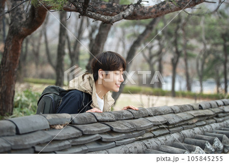 A young man wearing a camera and taking pictures while traveling to tourist attractions with traditional Korean houses	 105845255