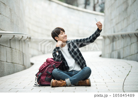 A young man traveling around a traditional village and taking pictures with a smartphone camera 105845489