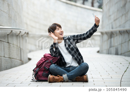 A young man traveling around a traditional village and taking pictures with a smartphone camera A young man traveling around a traditional village and taking pictures with a smartphone camera 105845490