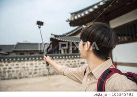 A young man traveling around a traditional village and taking pictures with a smartphone camera A young man traveling around a traditional village and taking pictures with a smartphone camera 105845493