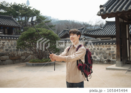 A young man traveling around a traditional village and taking pictures with a smartphone camera 105845494
