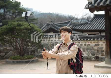 A young man traveling around a traditional village and taking pictures with a smartphone camera A young man traveling around a traditional village and taking pictures with a smartphone camera 105845495