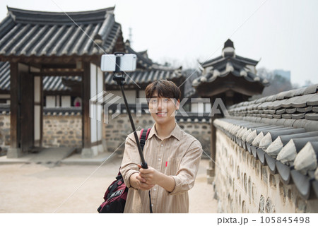 A young man traveling around a traditional village and taking pictures with a smartphone camera 105845498