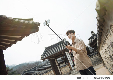 A young man traveling around a traditional village and taking pictures with a smartphone camera 105845499