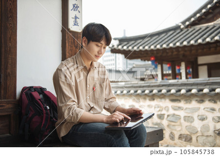A young man who uses a tablet while traveling in tourist attractions with traditional Korean houses 105845738