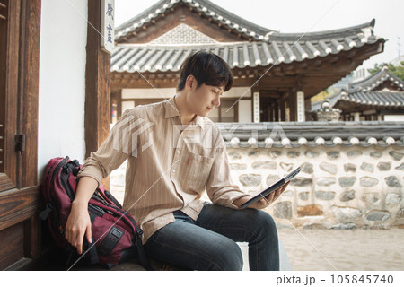 A young man who uses a tablet while traveling in tourist attractions with traditional Korean houses 105845740