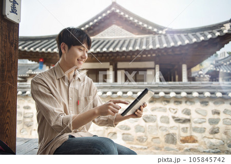 A young man who uses a tablet while traveling in tourist attractions with traditional Korean houses 105845742