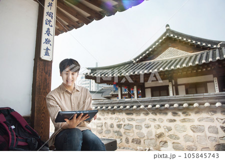 A young man who uses a tablet while traveling in tourist attractions with traditional Korean houses 105845743