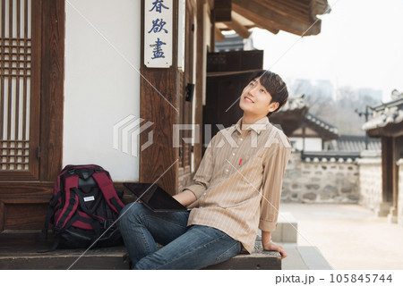 A young man who uses a tablet while traveling in tourist attractions with traditional Korean houses 105845744