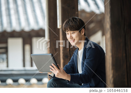 A young male college student sitting and looking at a tablet while traveling in Korea A young male college student sitting and looking at a tablet while traveling in Korea 105846158