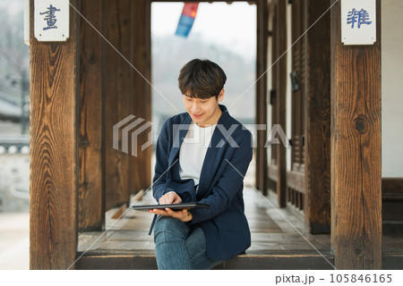 A young male college student sitting and looking at a tablet while traveling in Korea A young male college student sitting and looking at a tablet while traveling in Korea 105846165