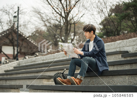 a young man sitting on the stairs looking at a map 105846585