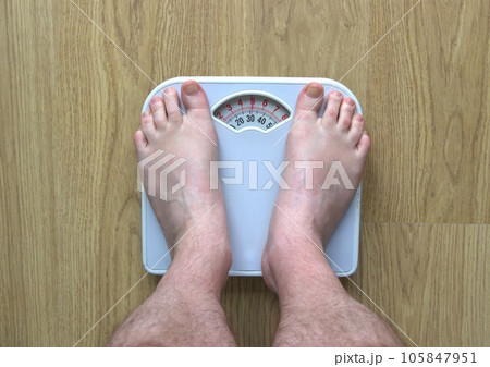 Man's feet standing on bathroom scales 105847951