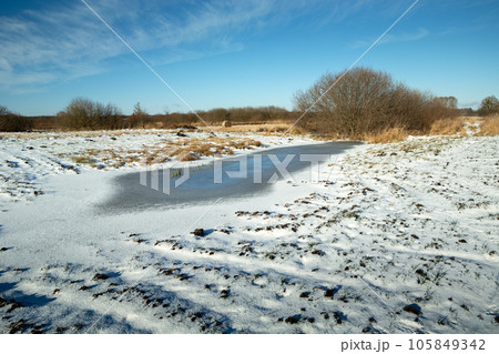 Winter landscape with a view of frozen water and snow on a plowed field, Eastern Poland Winter landscape with a view of frozen water and snow on a plowed field, Eastern Poland 105849342