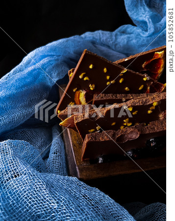 Pieces of chocolate with nuts and raisins on a dark background Pieces of chocolate with nuts and raisins on a dark background 105852681