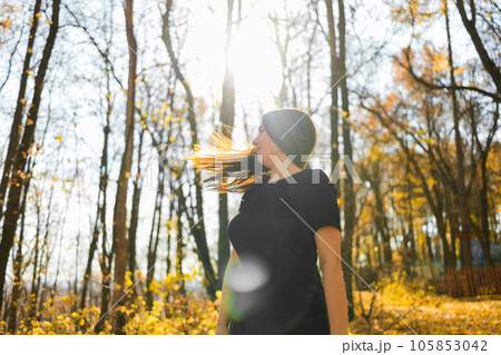 Cute young woman with long fluffy hair dancing in a park at sunset. Beautiful young woman with brown hair dance in a forest at sunset. Freedom and season nature concept. Soft focus 105853042