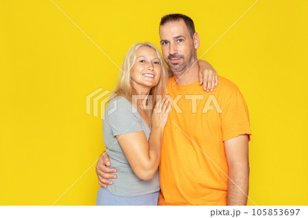 Caucasian real couple in their 40s embracing showing their love, isolated on yellow studio background. 105853697