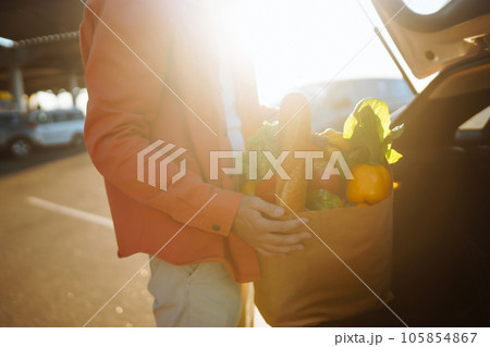 Young man with shopping bag full of vegetables near the car. Handsome man after shopping. 105854867
