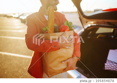 Young man with shopping bag full of vegetables near the car. Handsome man after shopping. Young man with shopping bag full of vegetables near the car. Handsome man after shopping. 105854878