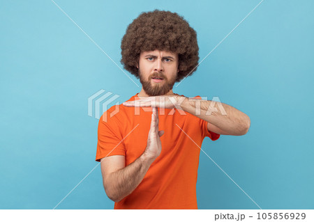 Portrait of serious man with Afro hairstyle wearing orange T-shirt showing timeout gesture, tired of lot of homework, extra classes. Indoor studio shot isolated on blue background. 105856929