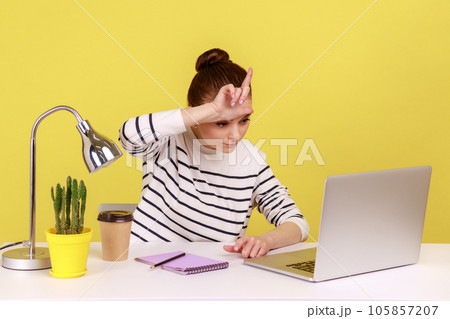 Lost job, unemployment. Depressed woman sitting at workplace with laptop and showing loser gesture, desperate about unlucky dismissal. Indoor studio studio shot isolated on yellow background. 105857207
