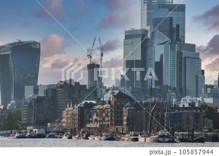 Sailing barge moored at harbor of Thames river. Modern skyscrapers with cloudy sky in background. Scenic view of capital city of London during sunny day. 105857944