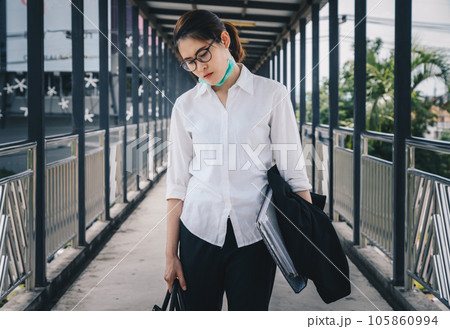 Absent-minded businesswoman walking on footbridge, stressed after laid off from work because impact from covid-19 pandemic outbreak. 105860994